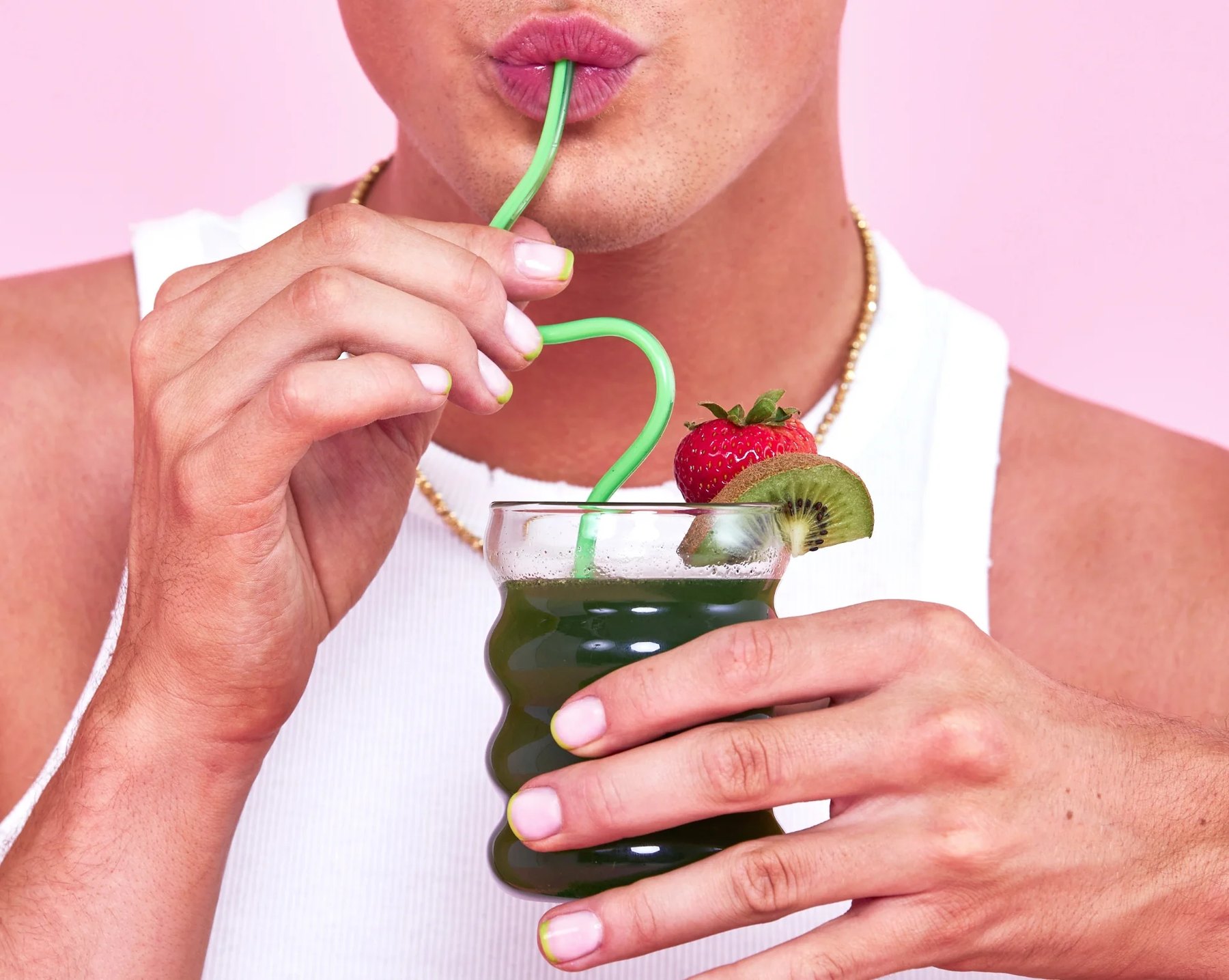 A person sipping strawberry kiwi greens garnished with fruit.