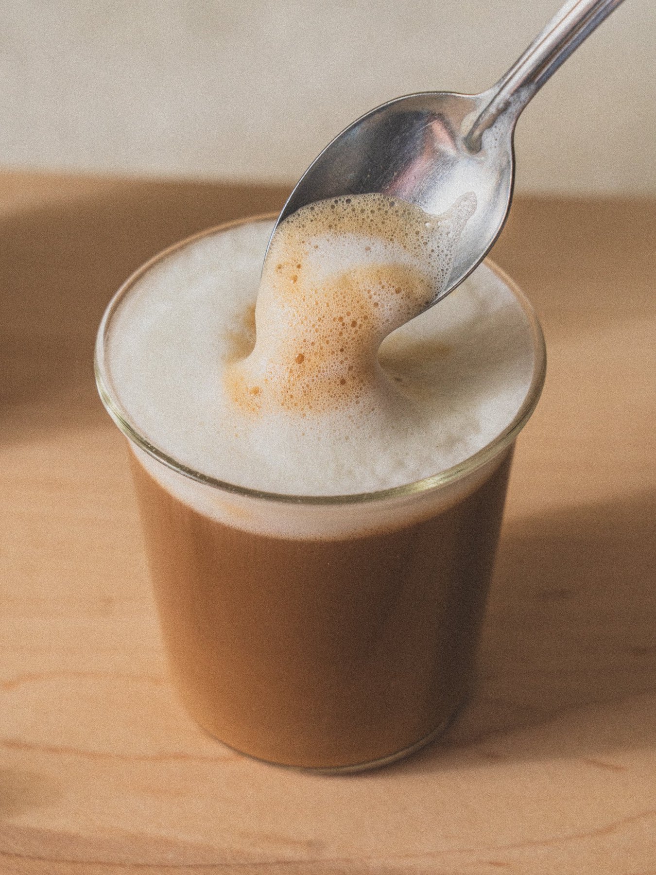 Close view of a frothy coffee drink being stirred with spoon.