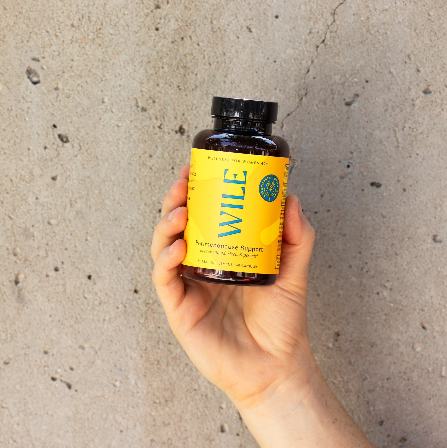Wile Perimenopause Support bottle held up before a concrete wall.